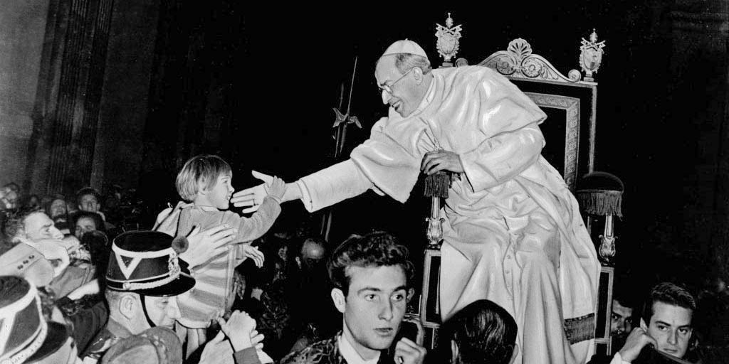 Papa Pio XII, sulla sedia gestatoria, saluta i parrocchiani durante un'udienza in Vaticano (Dominio Pubblico per decorso del tempo, fonte Wikimedia Commons)